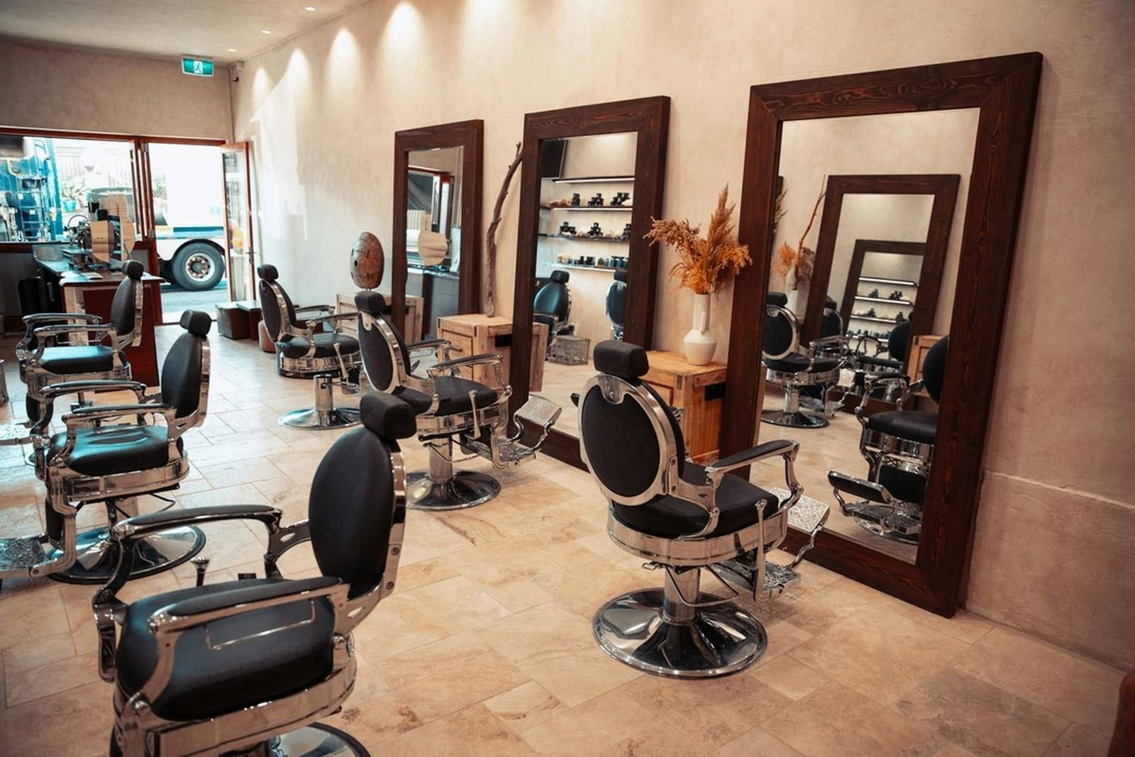 Barbearia com uma fila de cadeiras de barbeiro pretas em frente a espelhos de moldura de madeira